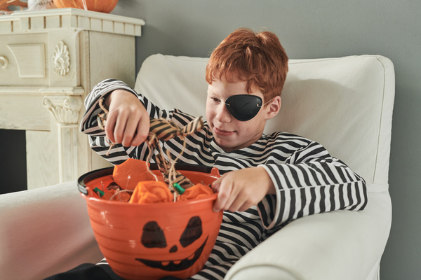 Boy in Pirate Costume Takes out Halloween Treat from Bucket with Painted Muzzle